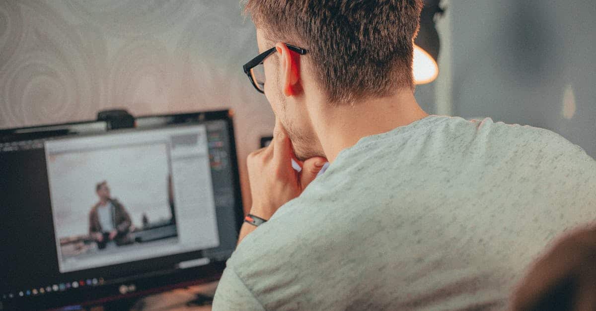 A man with glasses focused on editing a photo on his desktop computer in an office.